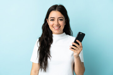 Fototapeta premium Young woman using mobile phone isolated on blue background smiling a lot