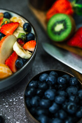 Close up of fruit salad in bowl next to heaps of blueberries and wooden chopping board with knife and fresh fruit