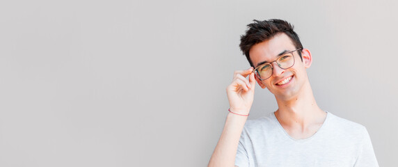 A portrait of young handsome man in grey t-shirt isolated on gray background touching his glasses.