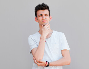 Young man with white shirt having doubts and with confuse face expression while scratching head on isolated grey background