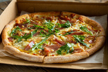 Pizza in the box.Pizza delivery.Pizza with cheese, jamon, arugula and pine nuts.Delicious hot pizza.Fast food at home.Home delivery of junk food.Pieces of in a box.Tasty food.Food with you.