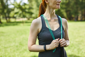 Close-up of active mature woman holding jump rope around neck in summer park