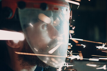Man welder grinder in transparent protective mask with flying sparks in darkness