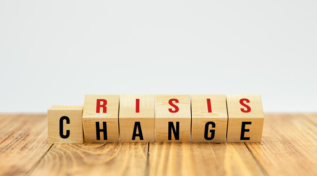 flipping cubes showing both words CRISIS and CHANGE at the same time on wooden table and white background