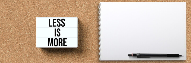 lightbox with message LESS IS MORE and notepad on cork background