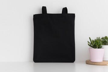 Black tote bag mockup with succulents on a white table.