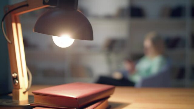Girl looking at smart phone sitting on a mesh at home at night. refocus on the table lamp