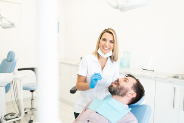 Fototapeta premium Smiling Dentist Examining Man in Dental Clinic
