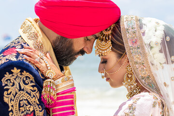 Sikh bride and groom posing on a tropical beach beneath bright blue skies