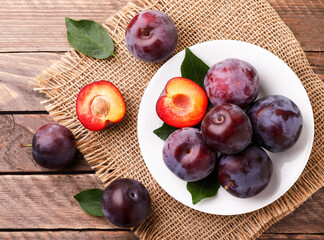 Ripe whole plums and half in a plate on a wooden background. The view from top