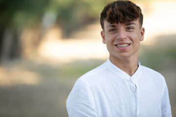 portrait of an Italian boy with short light hair with white shirt smiling in a park