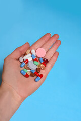 Close up shot of a hand holding color pills isolated on blue background, taking your medication.