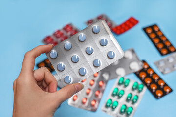 Close up of woman holding medicine pill in pack of blisters, pack of medicine pills and capsules on a blue background