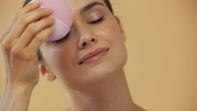Beautiful woman using silicone facial brash isolated on beige