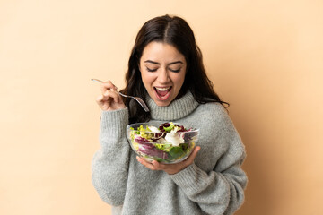 Young caucasian woman isolated on beige background holding a bowl of salad with happy expression