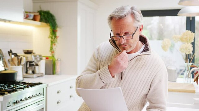 Mature man at home in kitchen drinking coffee and looking at paperwork relating to domestic finances and investments - shot in slow motion
