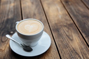 Fresh tasty coffee with beautiful latte art in white ceramic cup served on wooden table. Concept of hot morning beverage and lifestyle.