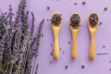 Dry lavender flower in wooden spoon and lavender bouquet on violet background