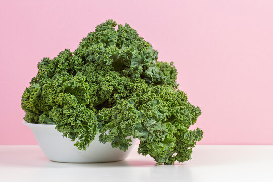 Fresh raw organic green curly kale leaves of kale on white plate with pink background
