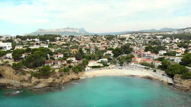 Distant aerial view rocky coves, sandy beach, tiny bay of Benissa. Turquoise bright blue Sea waters hillside townscape at sunny day. Drone point of view. Costa Blanca. Spain..