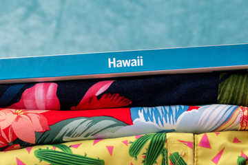 Concept for travel to tropical destinations such as Hawaii. Aloha shirts, colorful flower print fabrics, and travel accessories for a perfect holiday in paradise.