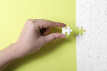 Woman putting last piece of white puzzle on yellow background, closeup