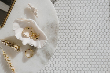 Minimal fashion composition with golden earrings in seashell on marble table with mirror and wheat stalks. Flat lay, top view bijouterie / jewelry concept on mosaic tile background. - obrazy, fototapety, plakaty
