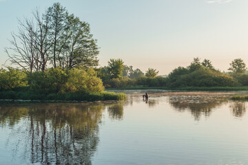 Summer landscape in Belarus. Colorful sky and reflections in the river at dawn. A man, a fisherman with a fishing rod crosses the river.