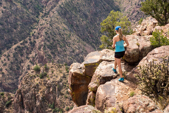 A fit young woman in shorts and tank top hikes along a cliff edge.