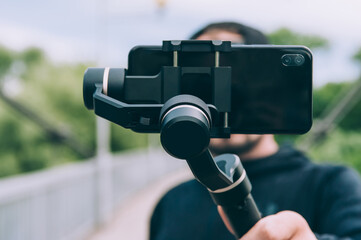 Blogger in nature shoots video on a smartphone with a manual camera stabilizer.