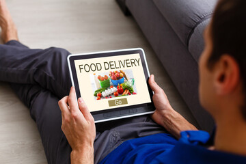 Man ordering take away food by internet with the tablet while lying at home.