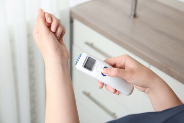 Woman measuring temperature with non contact infrared thermometer indoors, closeup