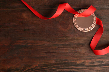Bronze medal with red ribbon on wooden background, flat lay. Space for design