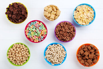 Various corn flakes in bowls on white wooden table