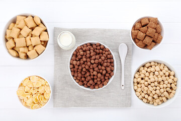 Various corn flakes with bottle of milk and spoon on white wooden table
