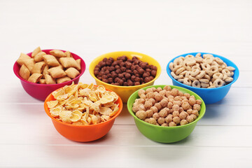 Various corn flakes in bowls on white wooden table