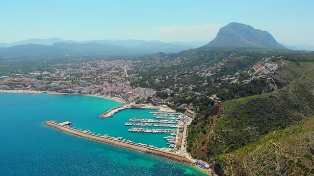 Aerial drone point of view coastal town of Javea with green mountains, turquoise bay Mediterranean Sea moored vessels in harbour, comarca of Marina Alta in province of Alicante, Valencia, Spain