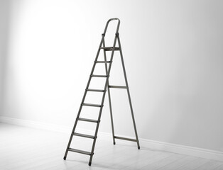 Modern metal stepladder near white wall indoors