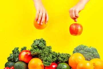 Hands picking apple and orange fruit from pile of fresh vegetables and fruits