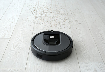 Modern robotic vacuum cleaner removing scattered buckwheat from wooden floor