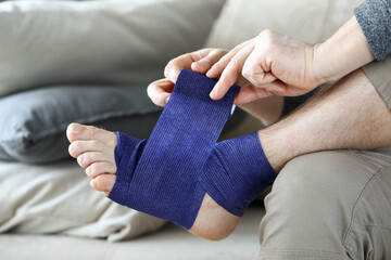Man sits at home couch and bandages foot bandage