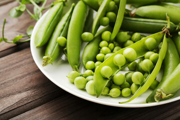 Green pea pods in plate on brown wooden table
