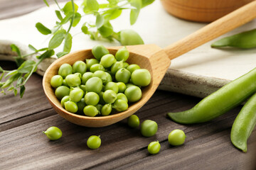 Fresh peas in spoon with green stem on brown wooden table