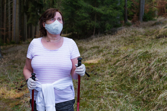 Senior woman is nordic walking in forest wearing coronavirus face mask. New normal, Self-isolation in the open air