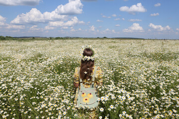 Russian fashionable girl with stylish vintage backpack. Field of wild camomiles. Flower field. Retro style in fashion. Summer day in Russia. July nature in countryside. Russian village. Flower wreath