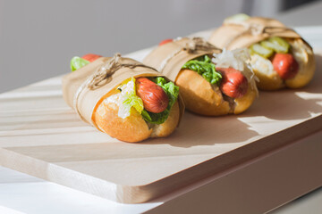 Three homemade hot dogs with cabbage, cucumbers and fresh green salad on a light wooden background.American fast Food in eco-packaging.National hot dog day.
