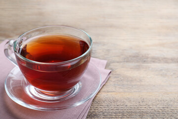 Cup of tasty black tea on wooden table. Space for text