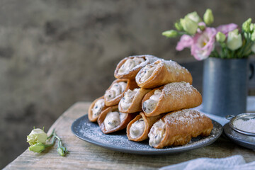 Sicilian cannoli deep fried pastry tubes on wooden rustic table with a sweet ricotta cream and dried candied fruits. Homemade Italian dessert on blue plate with flowers. Copy space, selective focus.