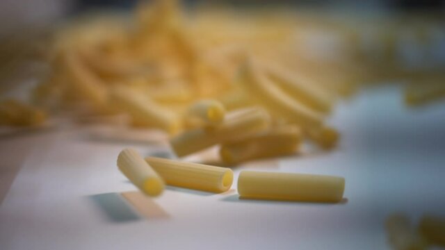 Close up of raw dried organic pasta macaroni running on a white conveyor belt in an Italian pasta factory. Healthy whole grain pasta. Food.