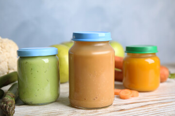 Jars with baby food and fresh ingredients on white wooden table